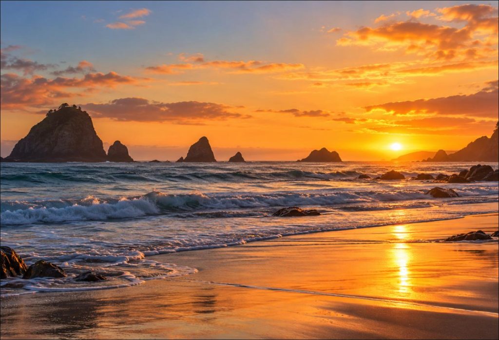 Golden hour sunset over a calm Pacific beach and sea stacks on the southern Oregon coast near Brookings