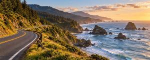 Coastal highway curving along green cliffs above the ocean and sea stacks at sunset